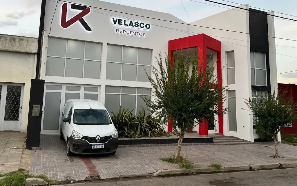 Fachada de Velasco Repuestos: edificio blanco con puerta roja